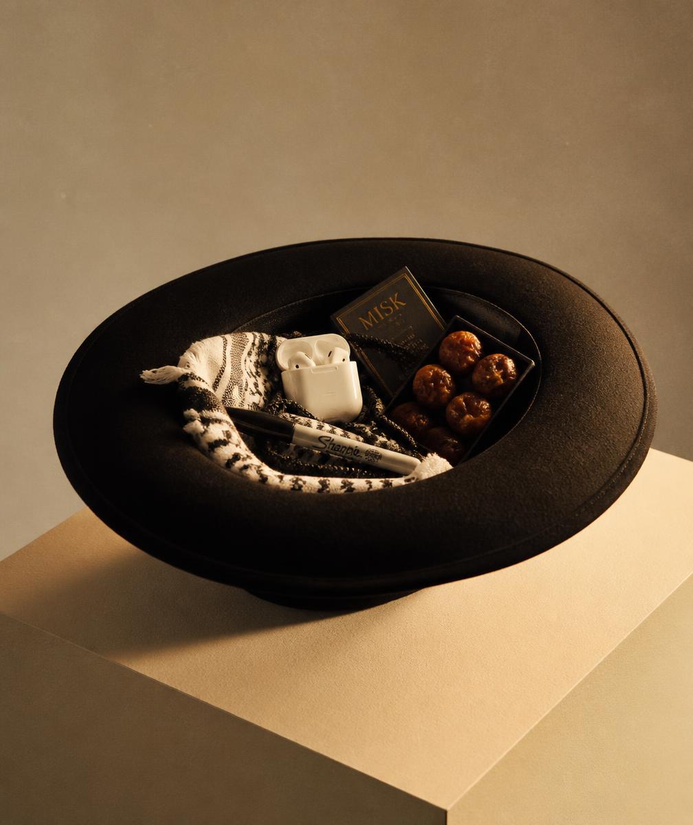 A matte black wide-brim hat holding earbuds, a folded shemagh, a marker and dates