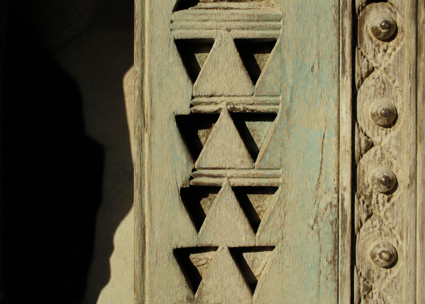 Close-up of a hand-carved Najdi door with triangular relief geometry and faded turquoise pigment