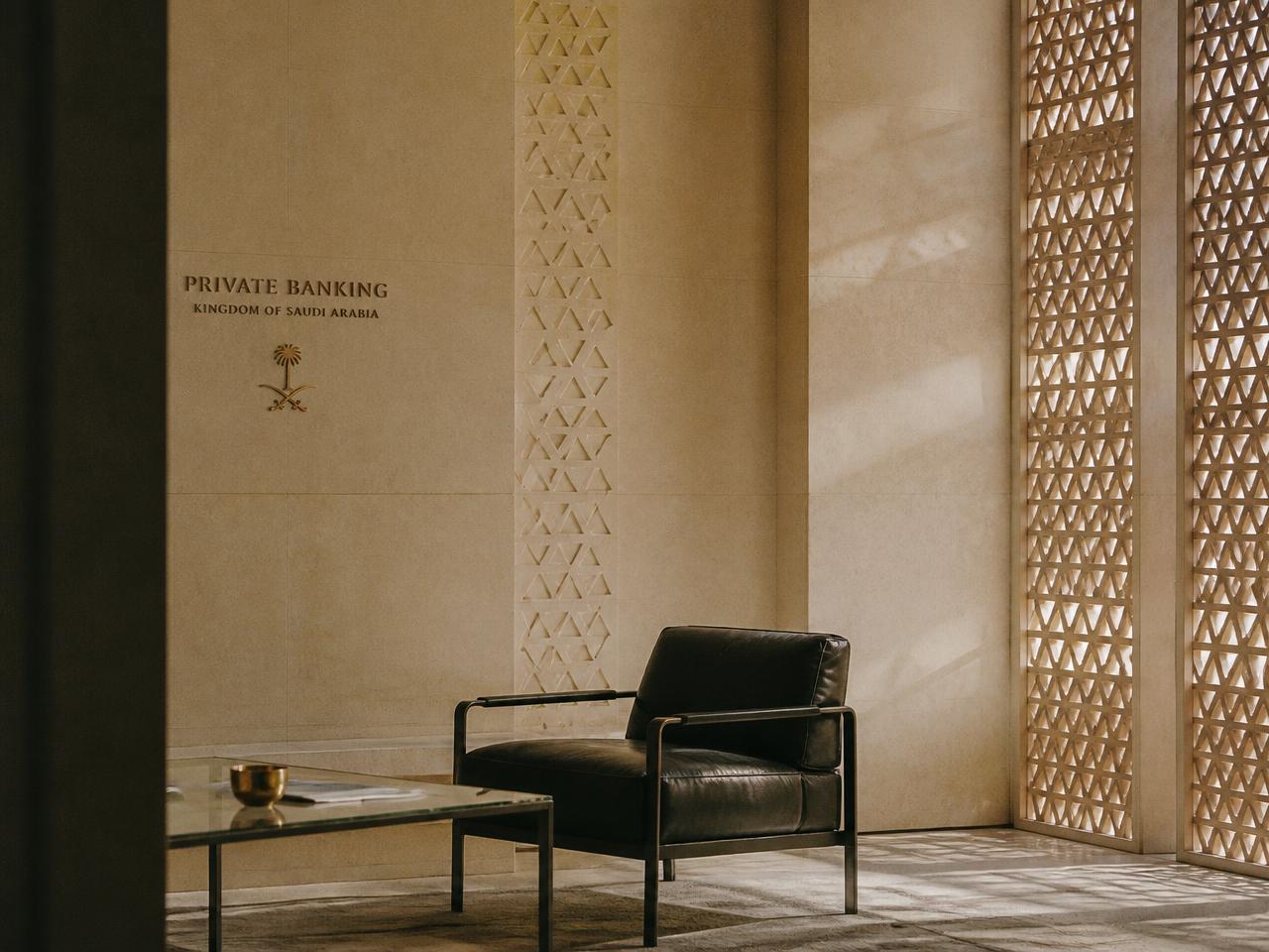 A quiet private banking lounge in Riyadh with Najdi relief stonework and gold afternoon light
